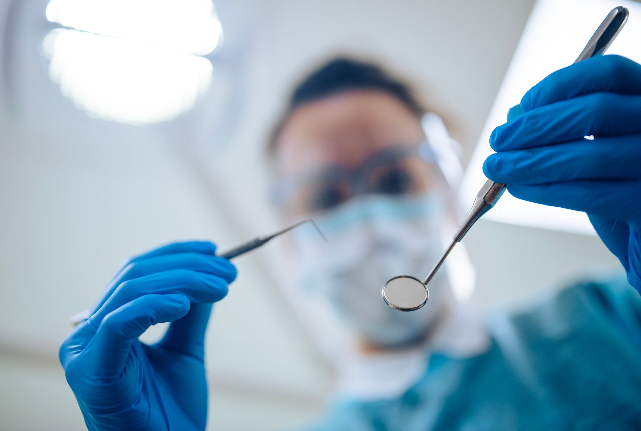 Dentiste tenant des instruments dentaires, arrière-plan flou. 